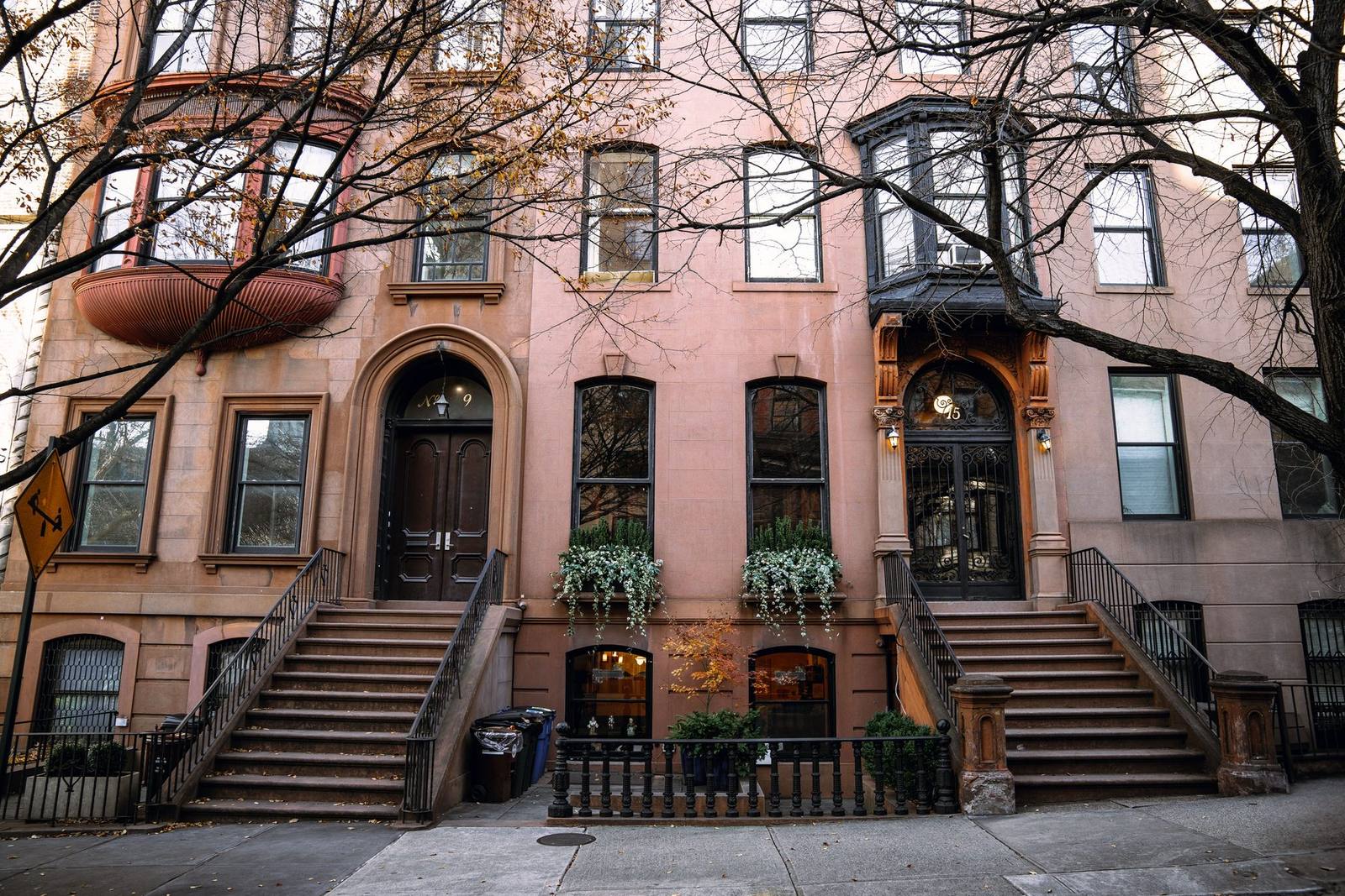 Brownstone building facades with wrought-iron stairs and trash bins on a Brooklyn block